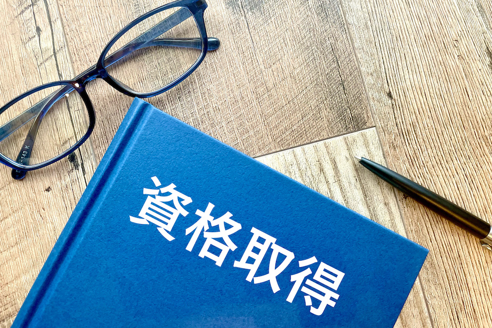 机に置かれたメガネと資格取得と書かれた本